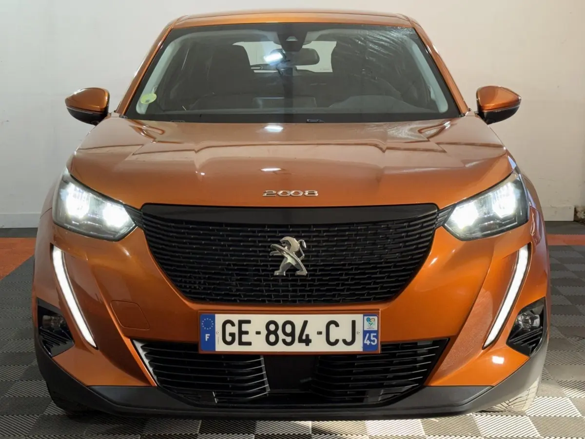 Vue avant d’un Peugeot 2008 orange 2022 avec phares allumés et calandre noire distinctive.