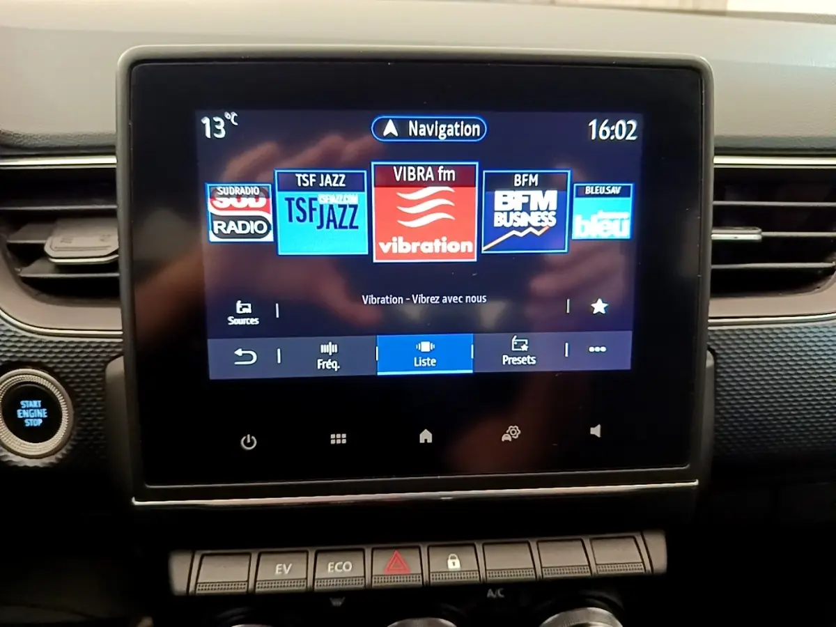 Écran tactile central de la Renault Arkana gris clair affichant les stations radio, avec bouton démarrage visible à gauche.