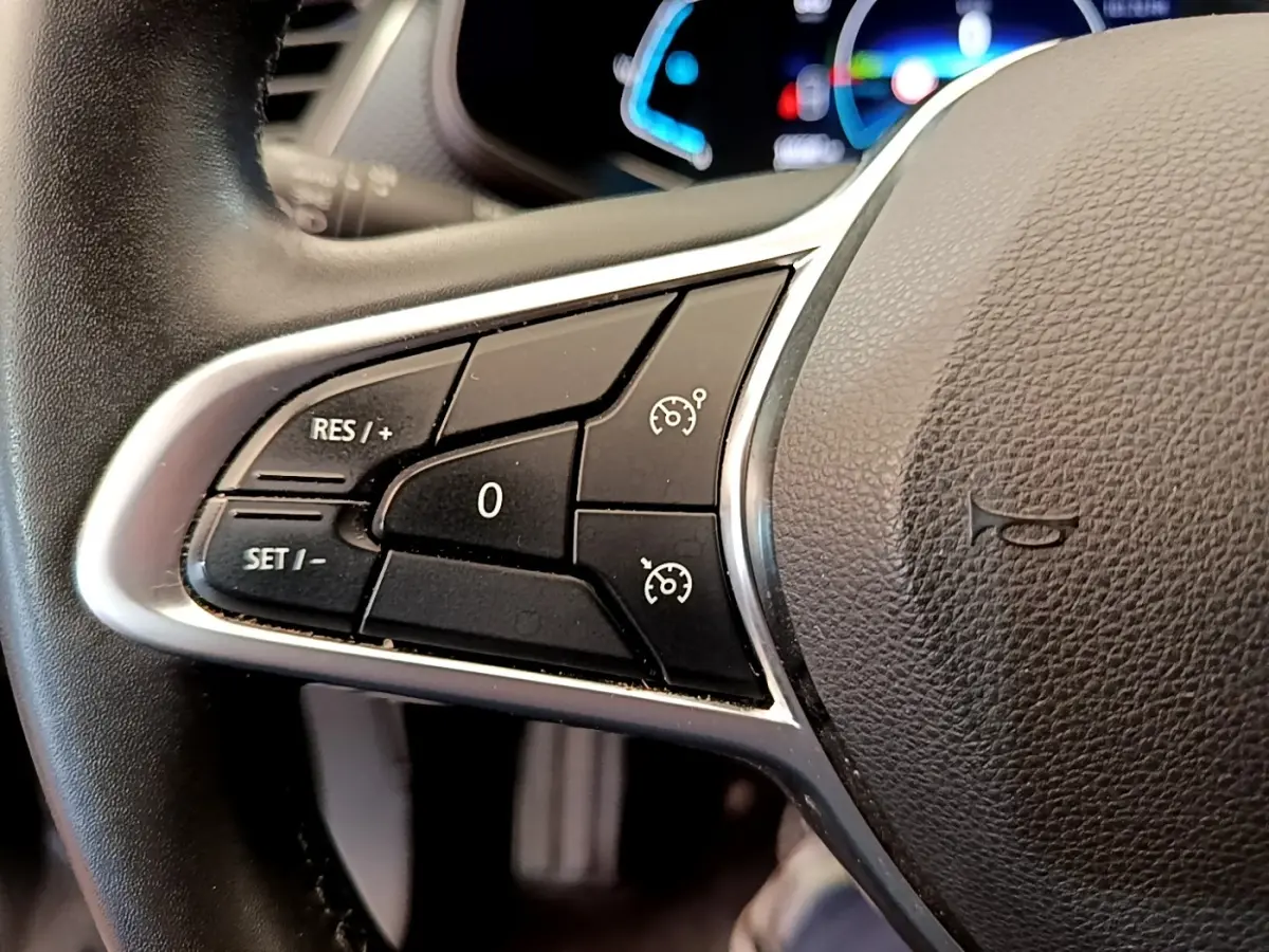 Gros plan sur les commandes de régulateur de vitesse au volant en cuir noir du Renault Arkana gris clair.