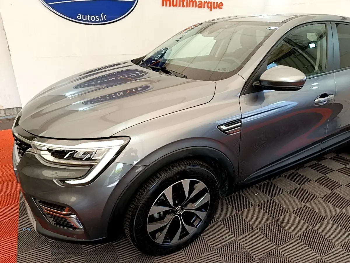 Vue 3/4 avant droit d’un Renault Arkana gris clair avec phares LED et jantes alliage distinctives.