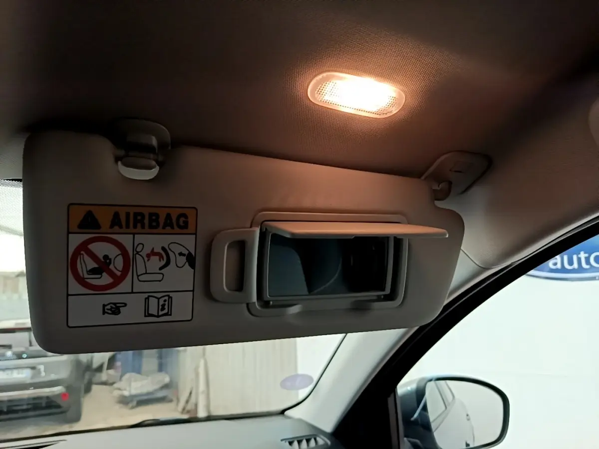 Détail intérieur montrant le pare-soleil côté conducteur gris clair avec miroir et avertissement airbag, éclairage allumé.