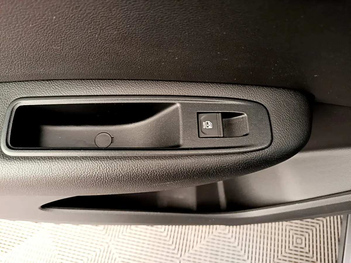 Gros plan sur la commande de lève-vitre noir dans la portière intérieure d'une Renault Arkana gris clair.