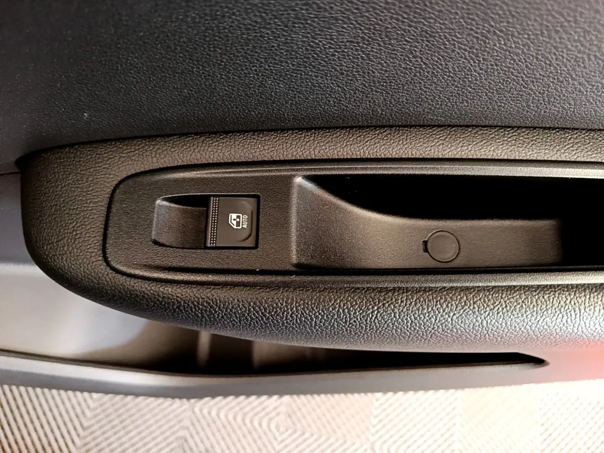 Gros plan sur la commande de lève-vitre côté conducteur dans l’habitacle noir du Renault Arkana gris clair.