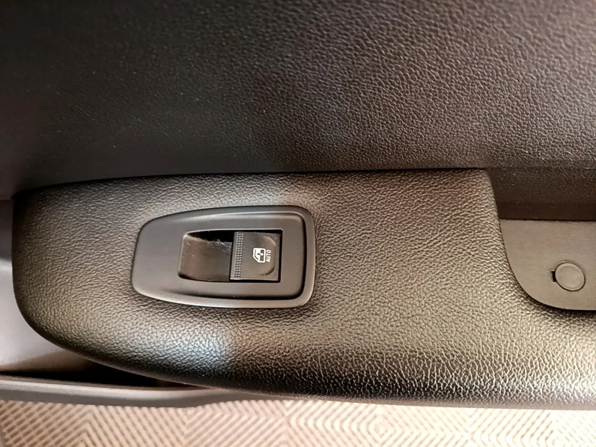 Gros plan sur le bouton de commande de la vitre électrique côté conducteur, intérieur noir texturé du Renault Arkana gris clair.