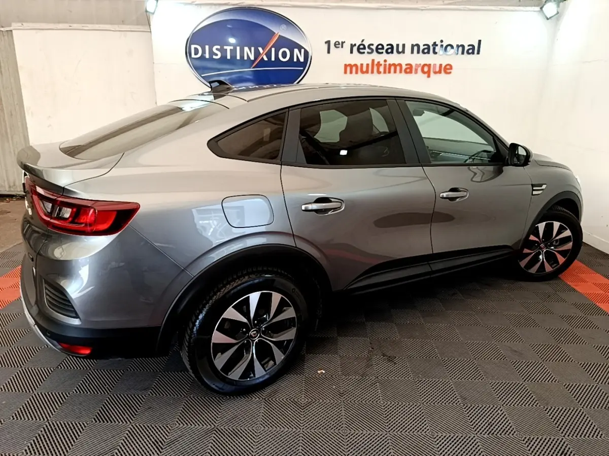 Renault Arkana gris clair en vue 3/4 arrière droit, soulignant ses lignes fluides et ses jantes bicolores modernes.