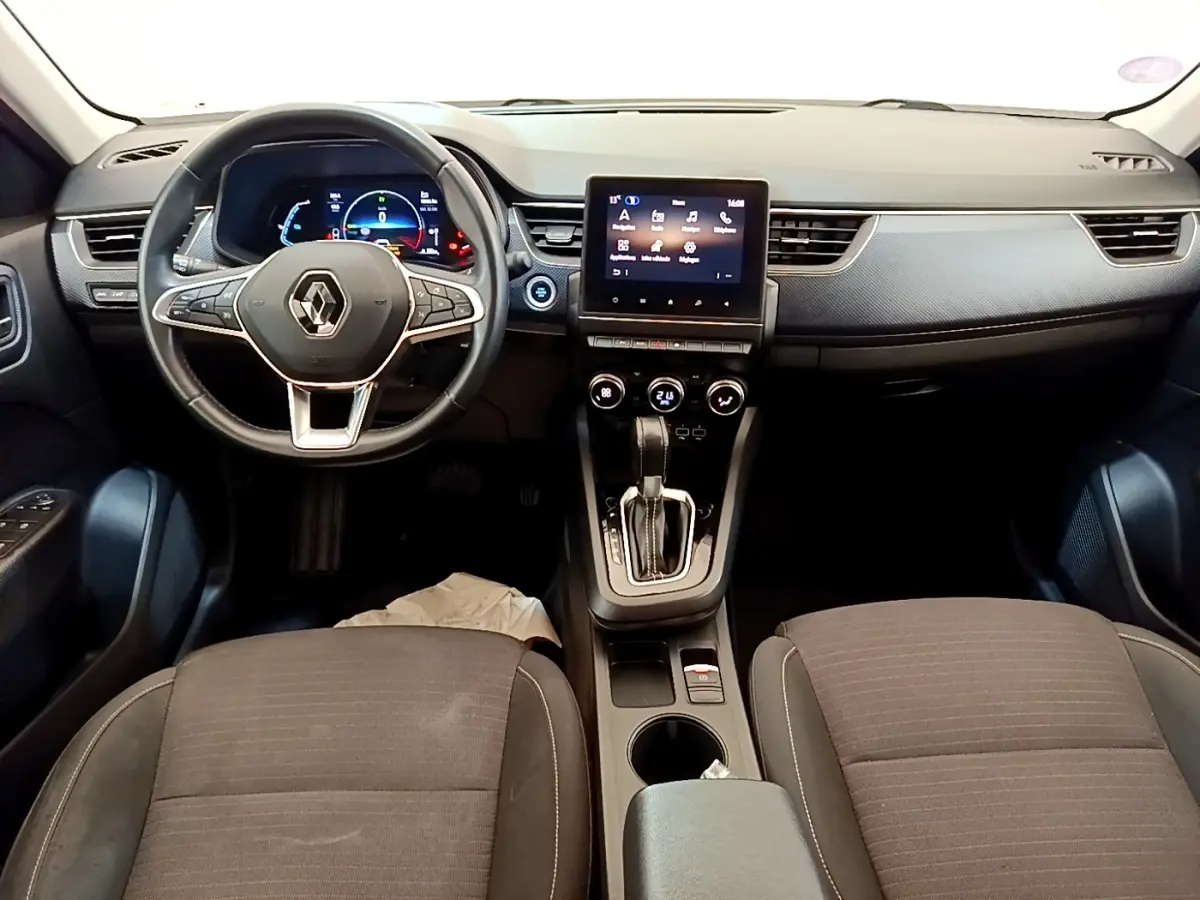 Vue intérieure avant du tableau de bord et volant noir de la Renault Arkana gris clair avec écran tactile central allumé.