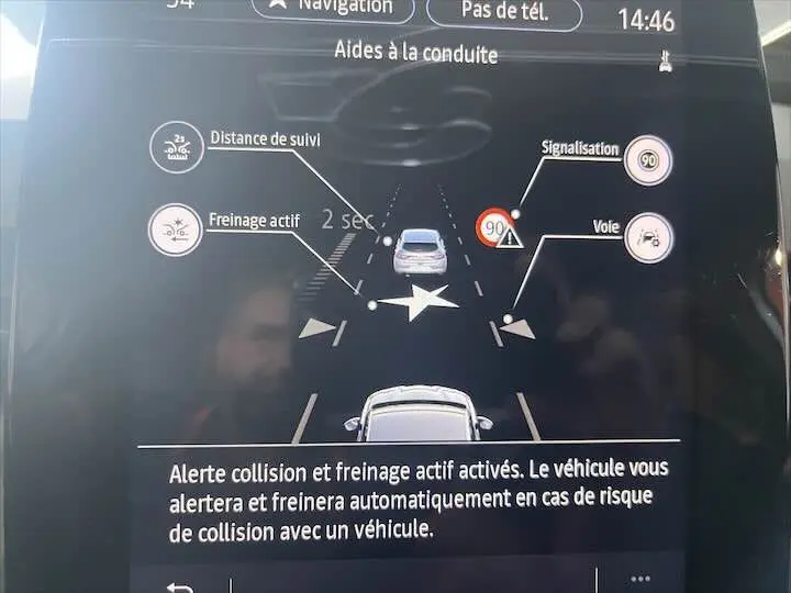 Affichage écran tableau de bord Renault Clio V blanc nacré, montrant l'alerte collision et freinage actif en conduite assistée.