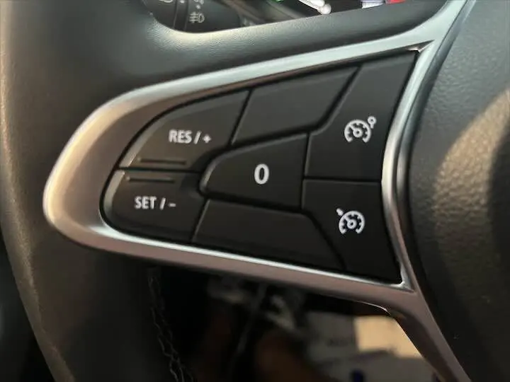 Gros plan sur les commandes de régulateur de vitesse au volant d'une Renault Clio V blanc nacré métal.