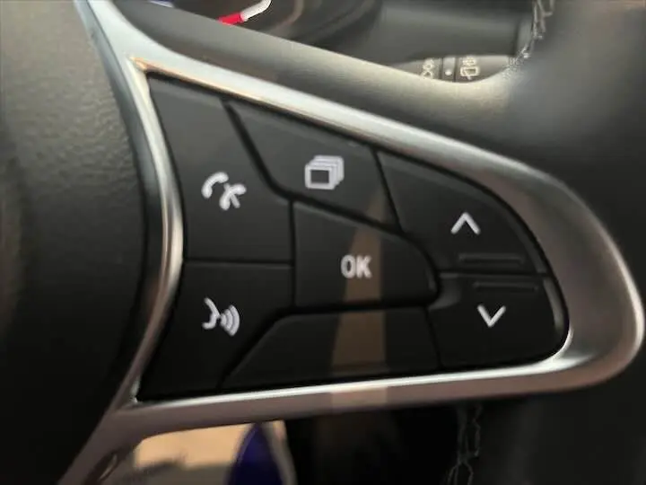 Gros plan sur les commandes au volant noir et argent de la Renault Clio V blanc nacré, boutons multifonctions avec flèches et OK.