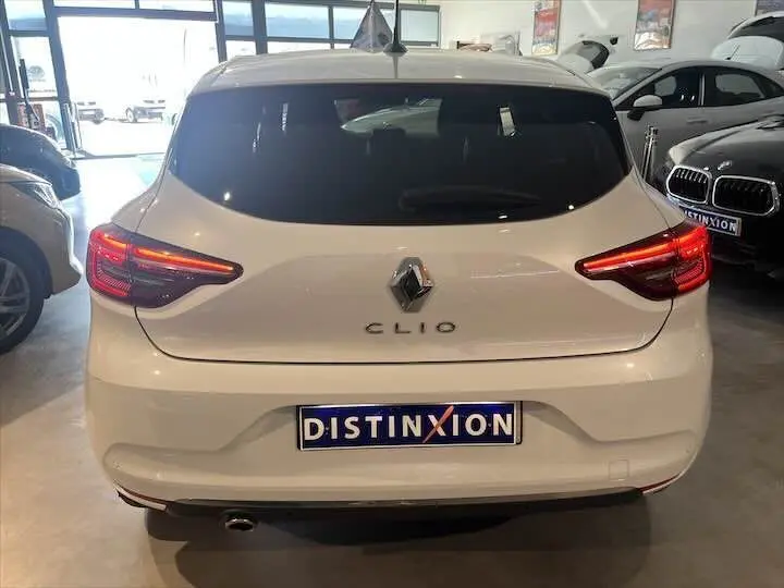Vue arrière d'une Renault Clio V blanche nacrée avec feux arrière allumés dans un showroom.