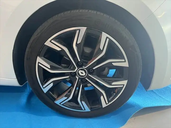 Gros plan sur la roue avant droite d'une Renault Clio V blanc nacré avec jante alliage noire et argentée au design moderne.