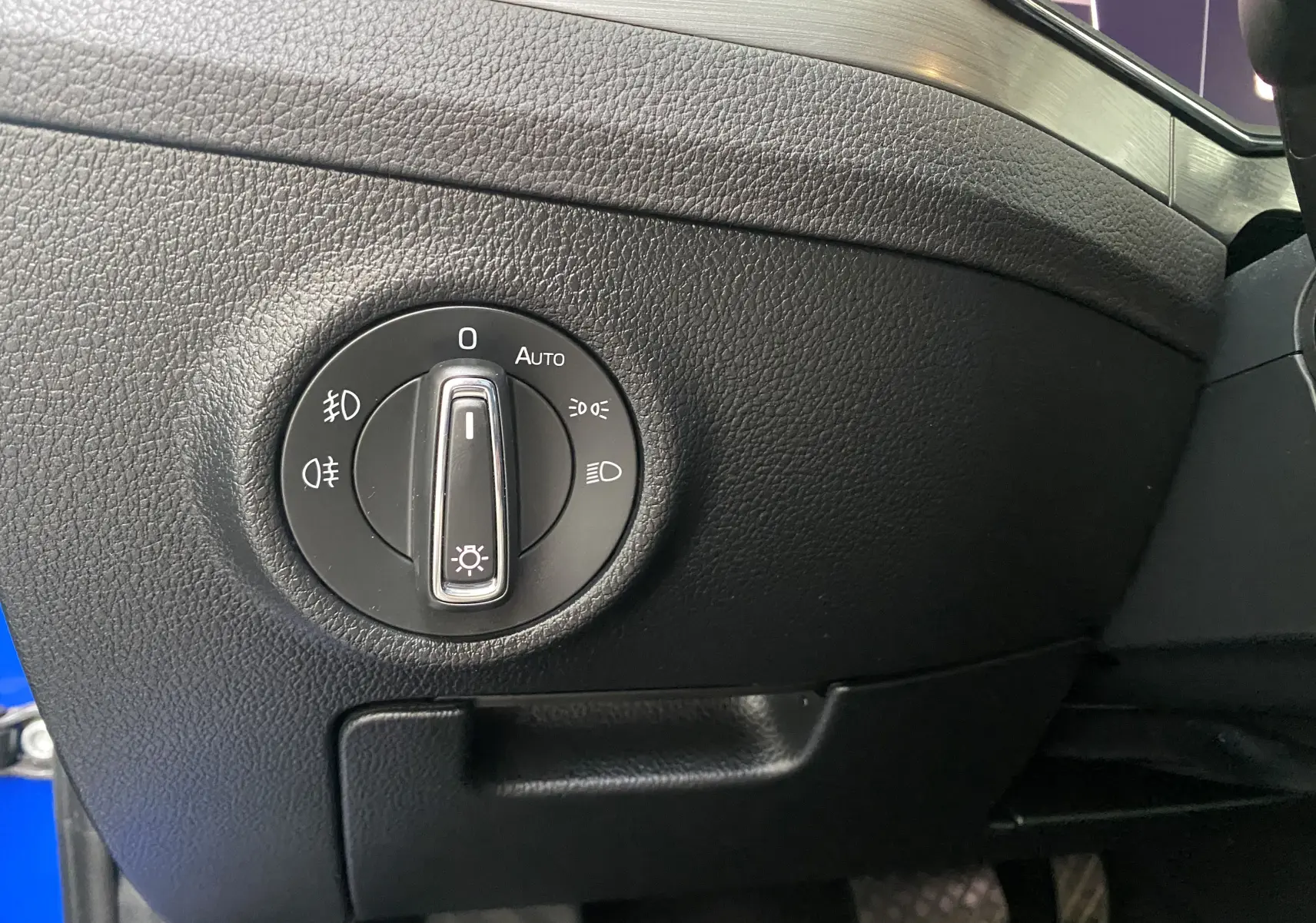Gros plan sur le bouton de commande des phares dans l'habitacle noir d'une Skoda Superb Combi bleu énergie de 2020.