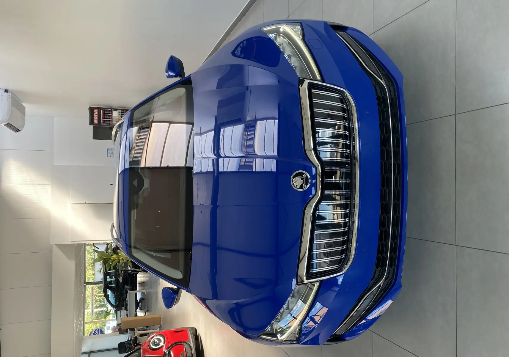 Vue avant plongeante d'une Skoda Superb Combi bleu énergie dans un showroom, soulignant sa calandre chromée et ses phares LED.