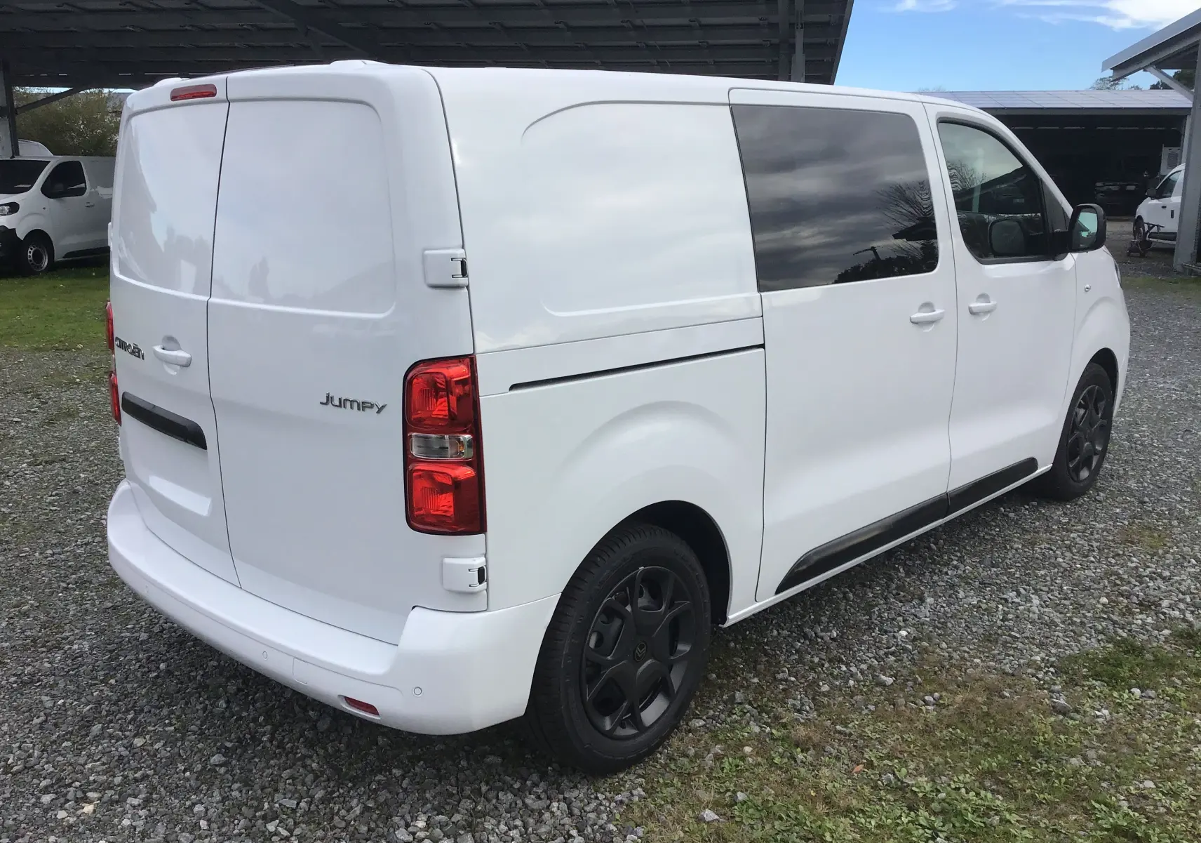 Vue 3/4 arrière droite d'un Citroën Jumpy cabine approfondie blanc avec vitres teintées et jantes noires.