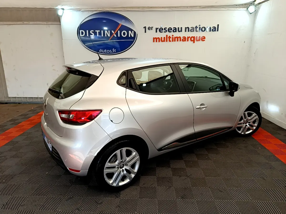 Renault Clio Business TCe 90 gris clair vue 3/4 arrière droit dans un showroom avec logo Distinxion en arrière-plan