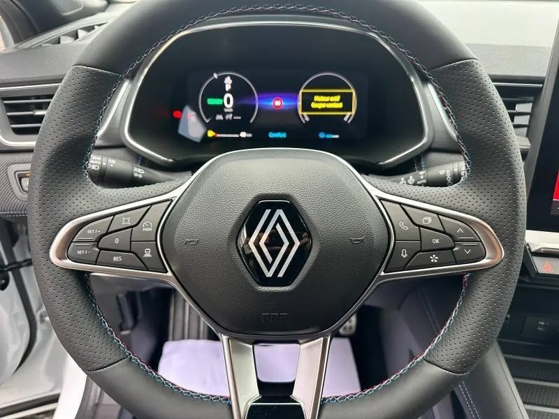 Vue rapprochée du volant perforé avec logo Renault et tableau de bord numérique du Captur hybride 2025 esprit Alpine.