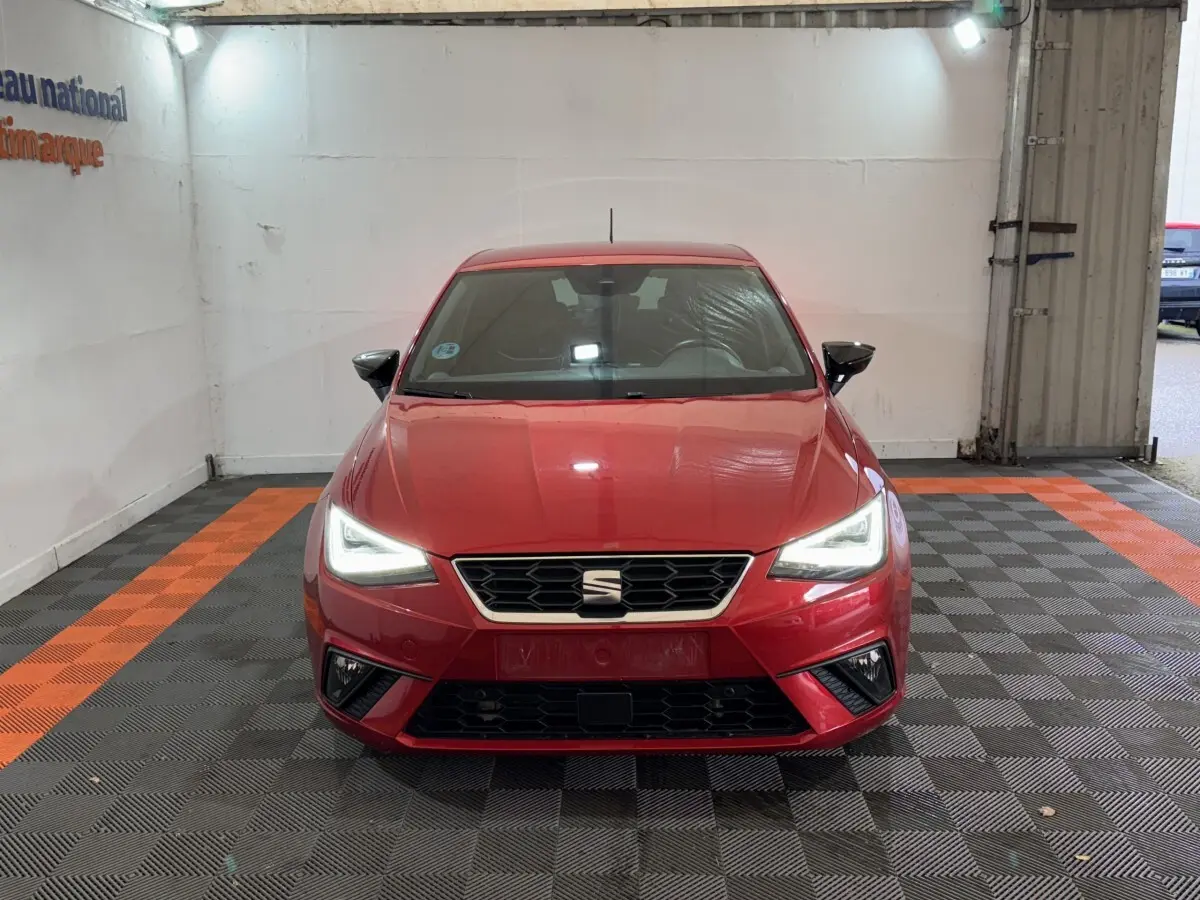 Vue frontale d'une SEAT Ibiza 1.0 TSI 110 FR rouge avec phares LED allumés dans un garage.