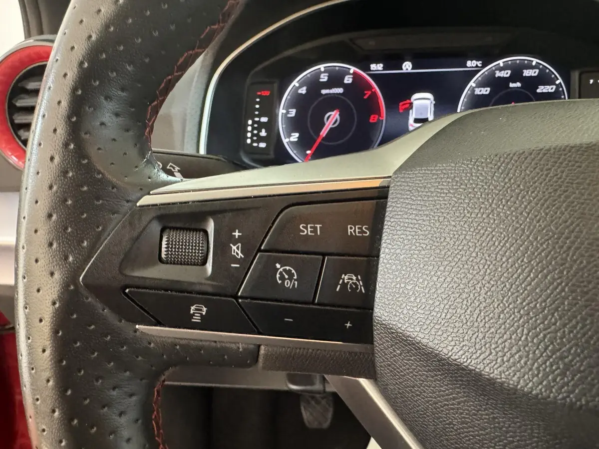 Gros plan sur le volant cuir perforé côté gauche de la SEAT IBIZA rouge 2024 avec commandes régulateur et assistance active.