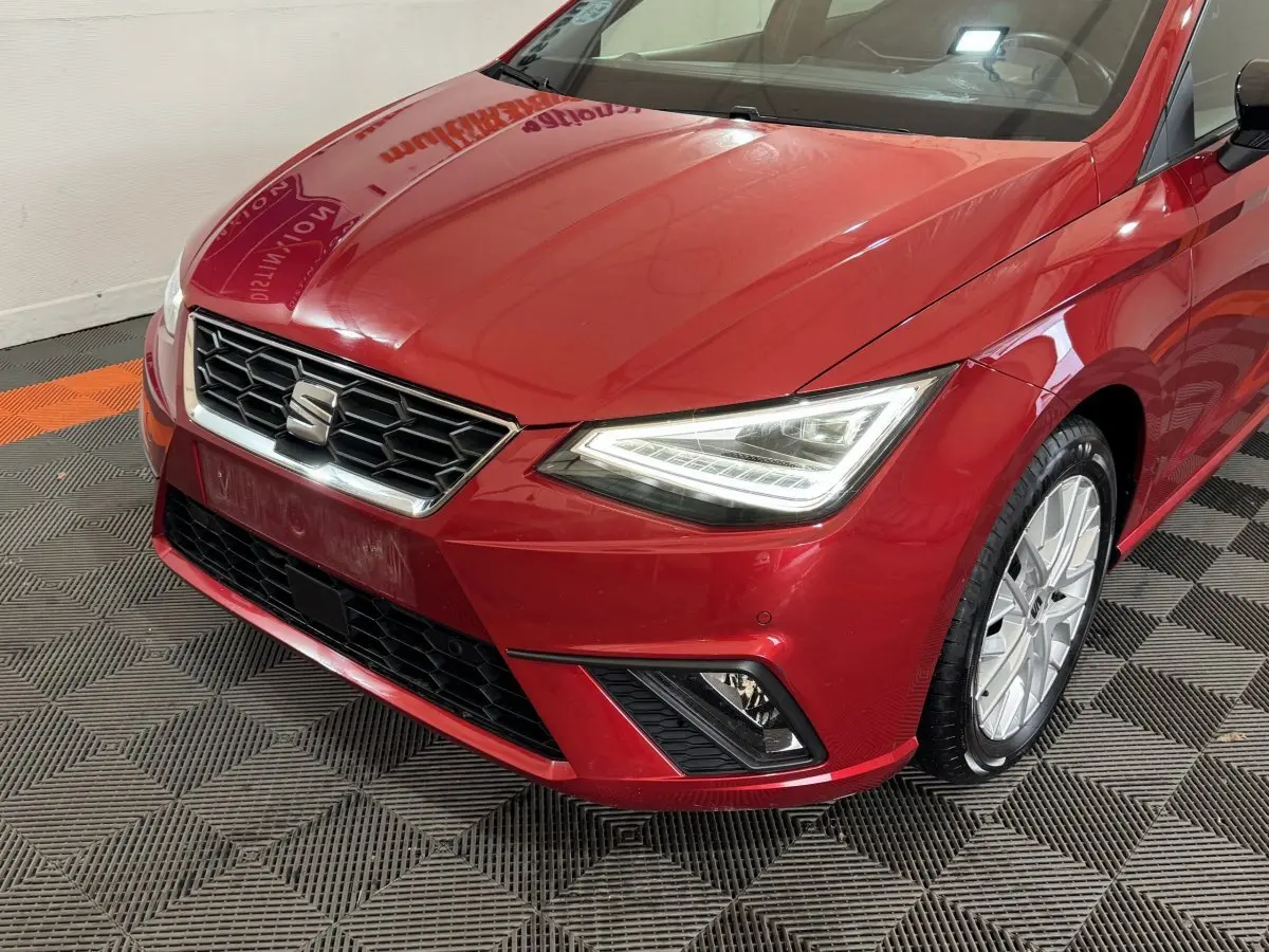 Vue 3/4 avant droit d'une SEAT IBIZA 1.0 TSI 110 FR rouge avec phares LED et calandre hexagonale chromée.