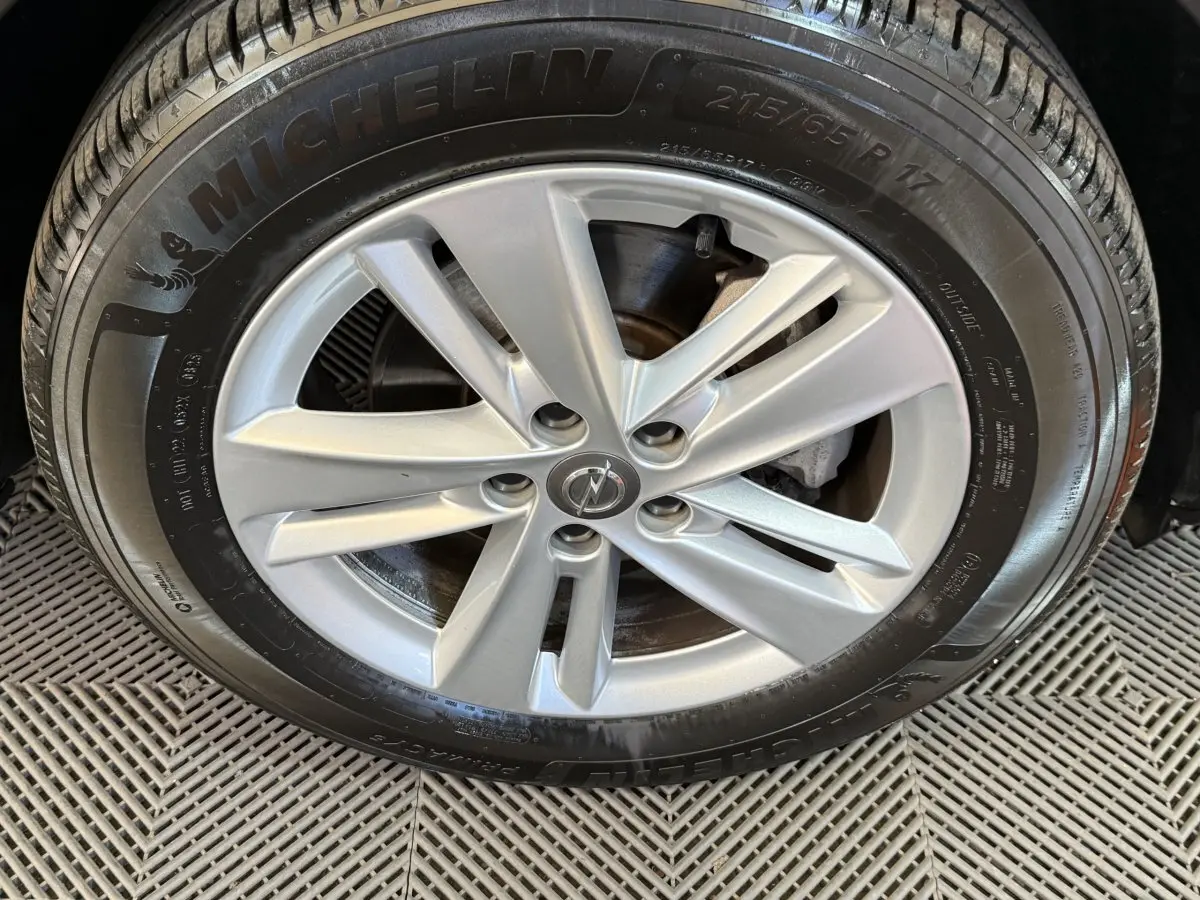 Gros plan sur la roue avant droite d’un Opel Grandland X noir, jante alliage argentée avec logo Opel central.