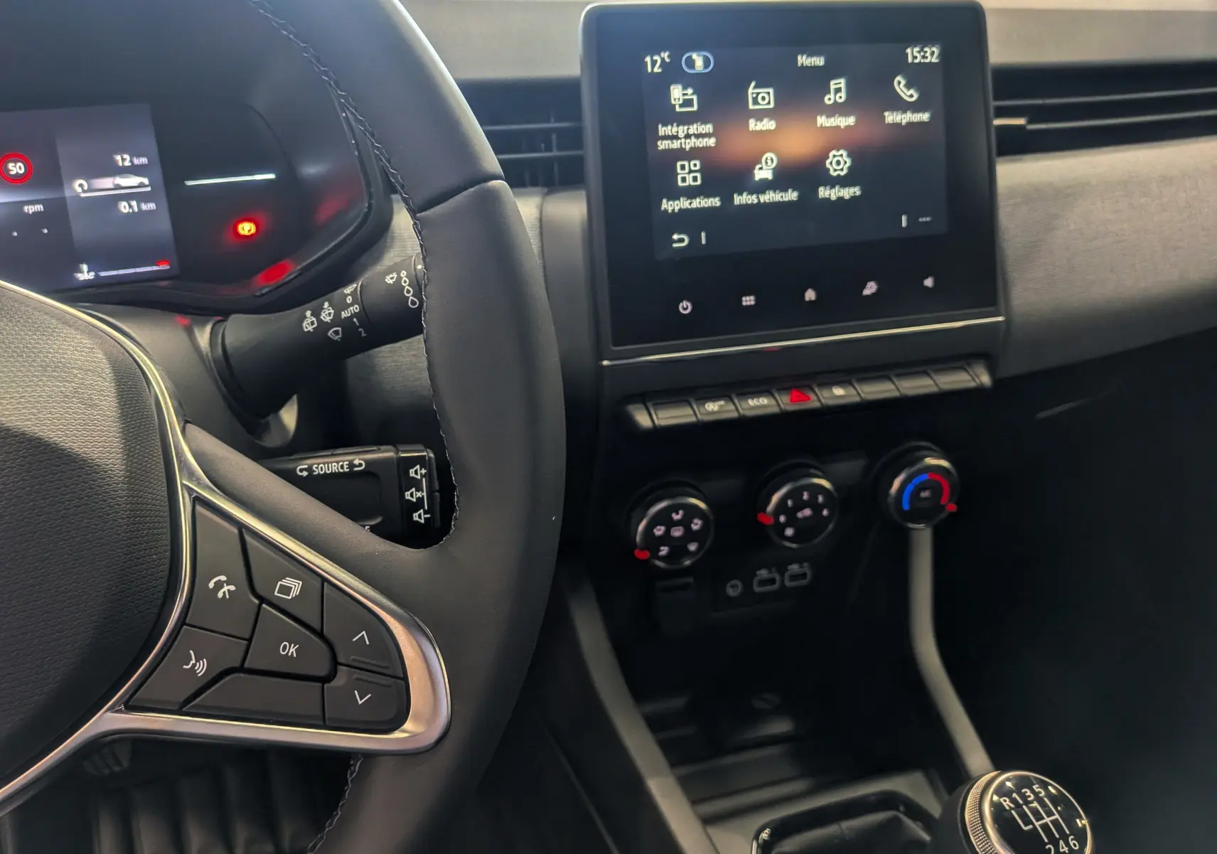 Vue intérieure rapprochée côté conducteur de la Renault Clio V Bleu Iron, avec volant, écran tactile et levier de vitesse manuel visible.