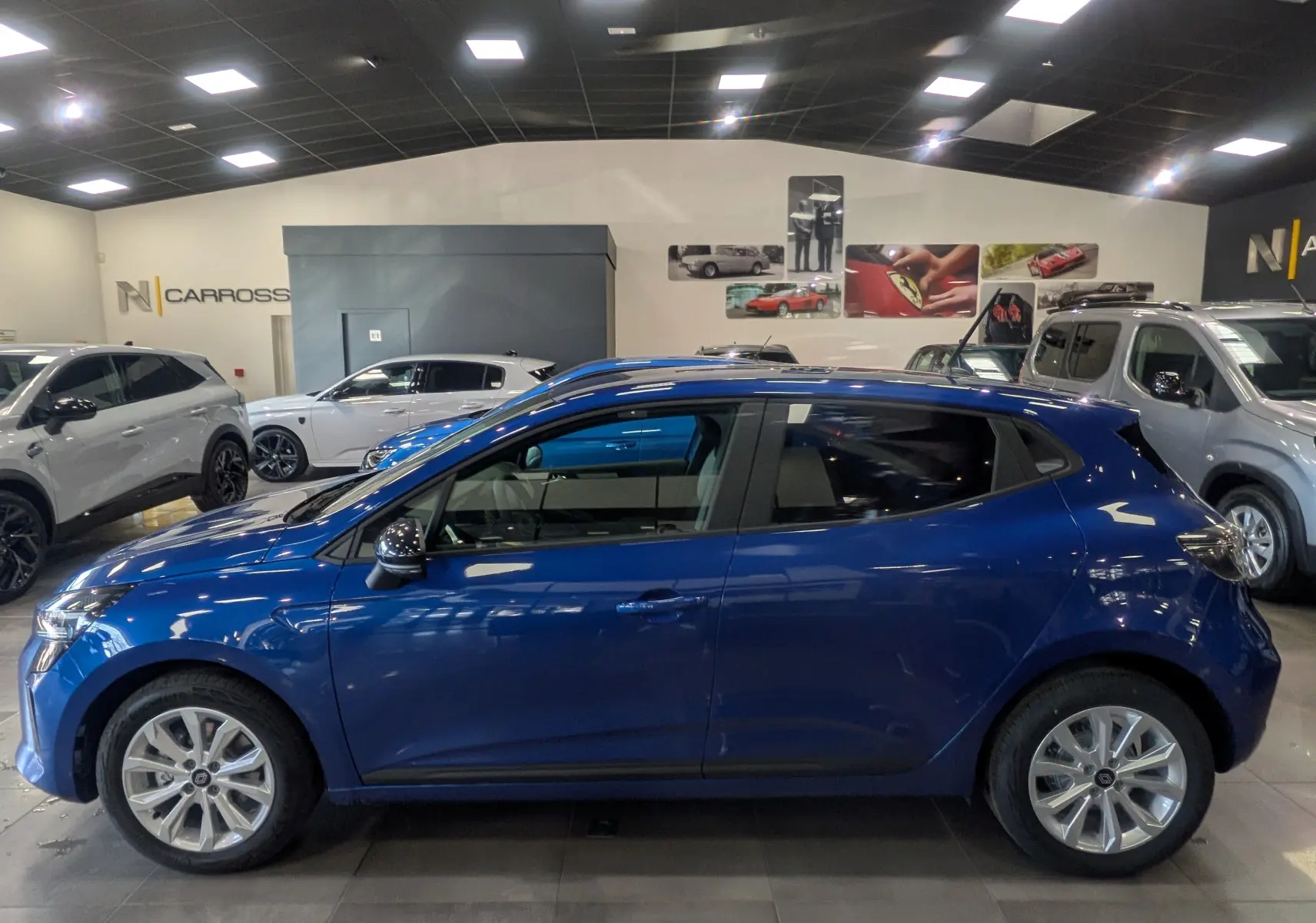 Profil côté gauche d'une Renault Clio V bleu Iron 2025 en version Blue dCi 100 CH Evolution, en intérieur showroom.