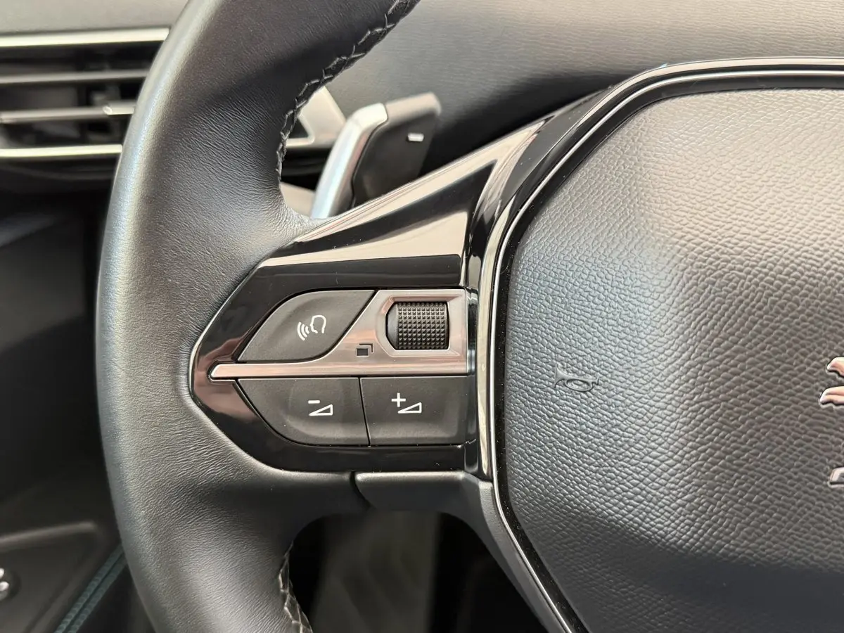 Gros plan sur les commandes gauche du volant cuir noir du Peugeot 3008 gris foncé, avec boutons multifonctions.