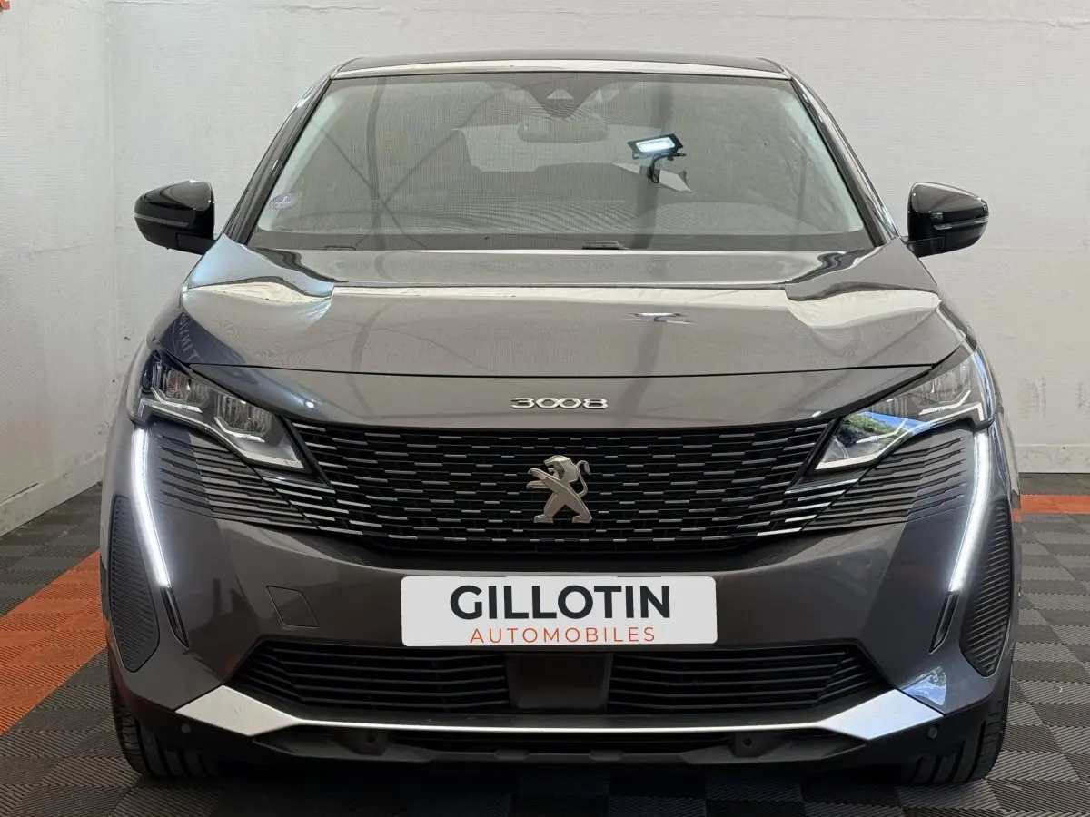 Vue frontale d’un Peugeot 3008 gris foncé avec calandre noire et feux LED verticaux allumés.