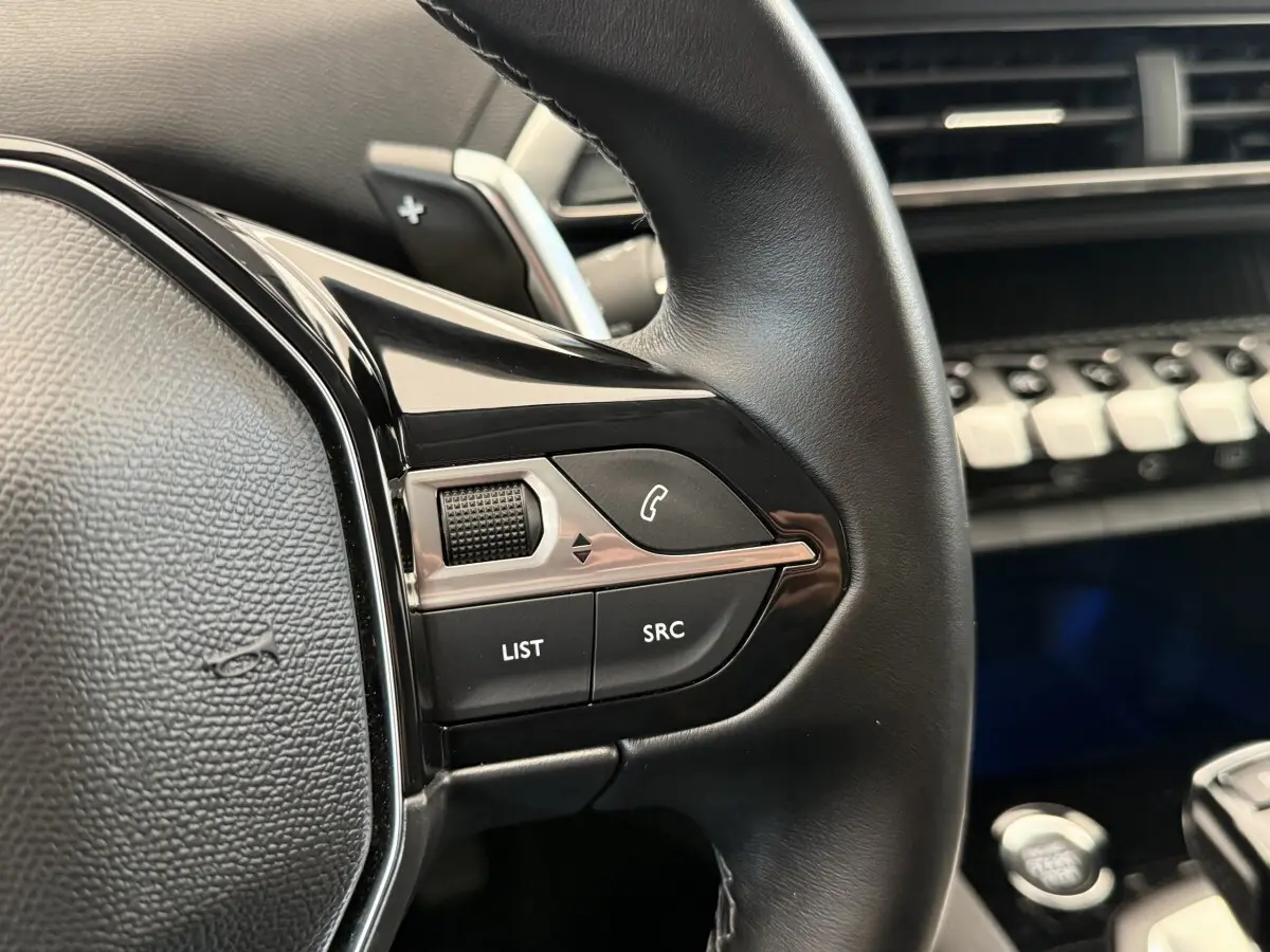 Gros plan sur les commandes gauche du volant cuir noir du Peugeot 3008 2022, avec tableau de bord en arrière-plan.