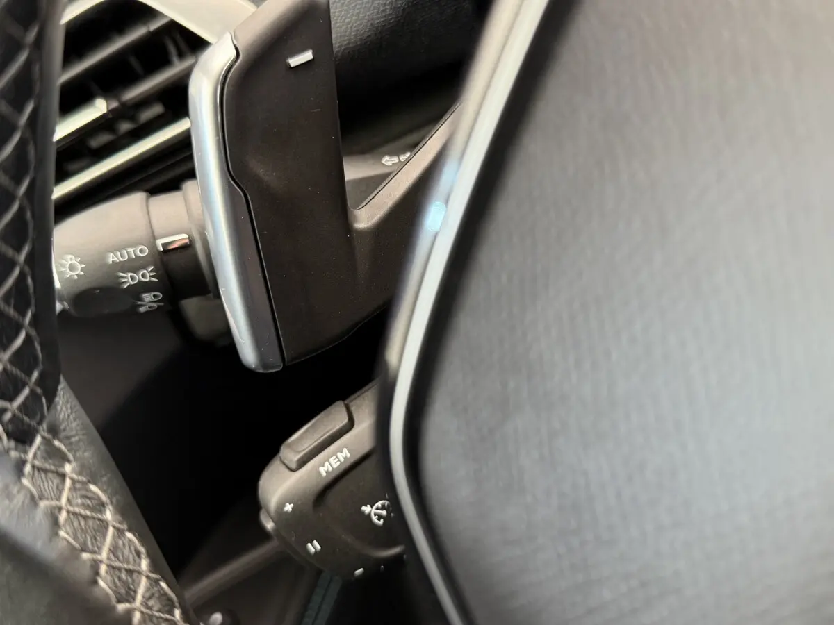 Détail du volant cuir noir et des commandes multifonctions du Peugeot 3008 PureTech 130 gris foncé, vue rapprochée.