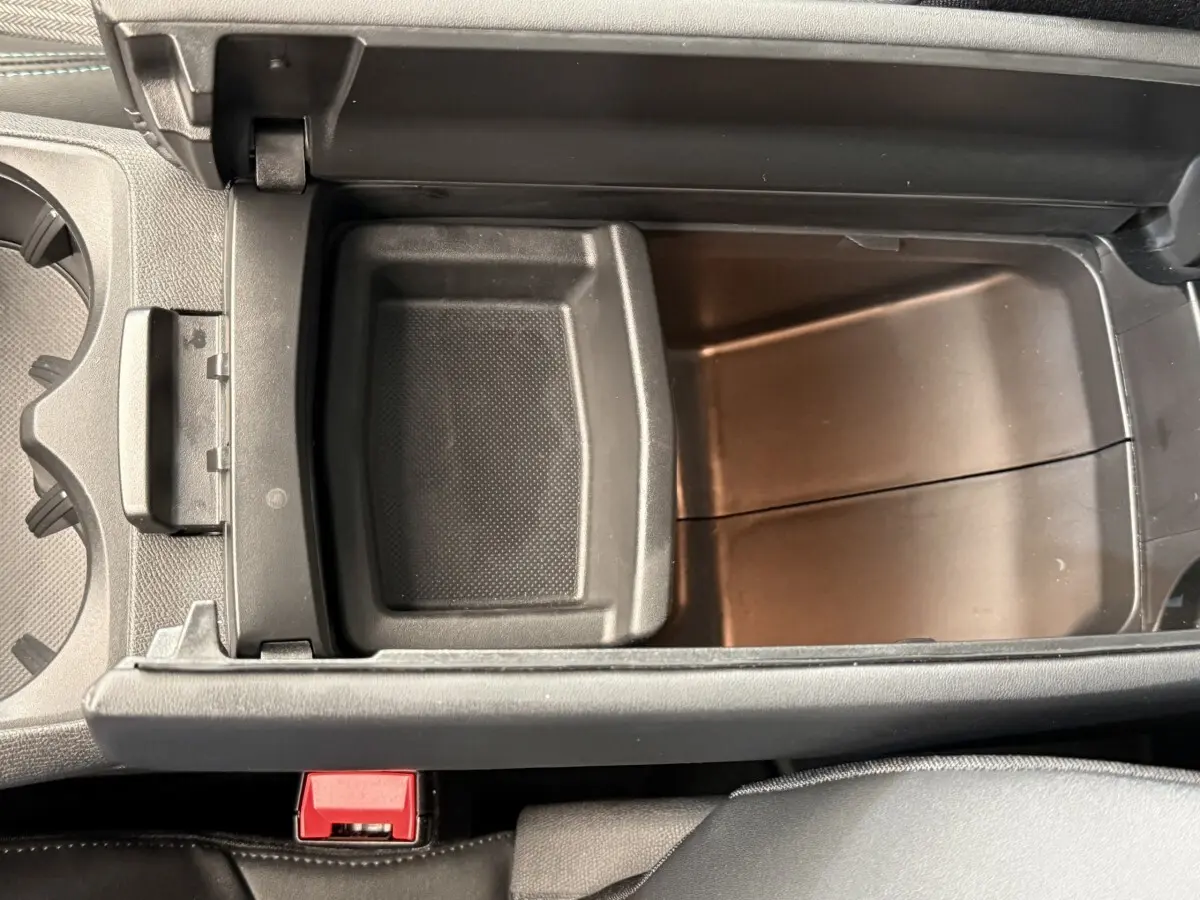 Vue plongeante sur le rangement central ouvert du Peugeot 3008 gris foncé, avec compartiment intérieur et bouton rouge visible.