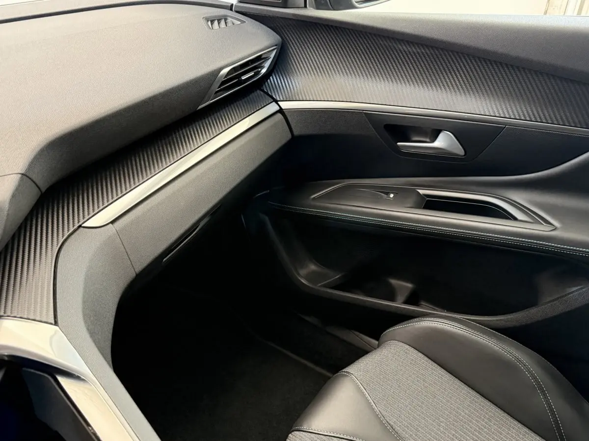 Vue intérieure côté passager du Peugeot 3008 gris foncé, mettant en valeur la planche de bord et la porte avec finitions noires et surpiqûres blanches.