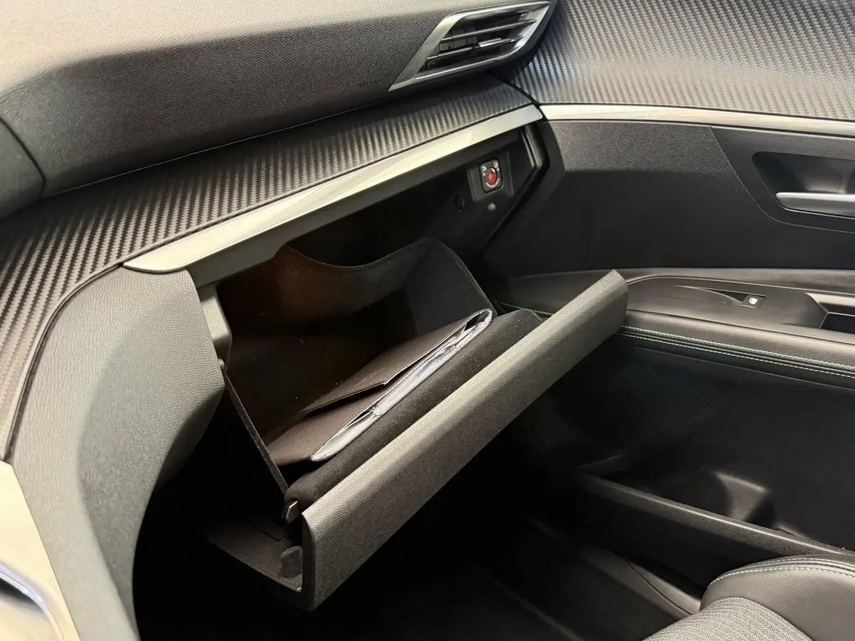 Vue intérieure côté passager du Peugeot 3008 gris foncé 2022 avec boîte à gants ouverte et finition carbone.