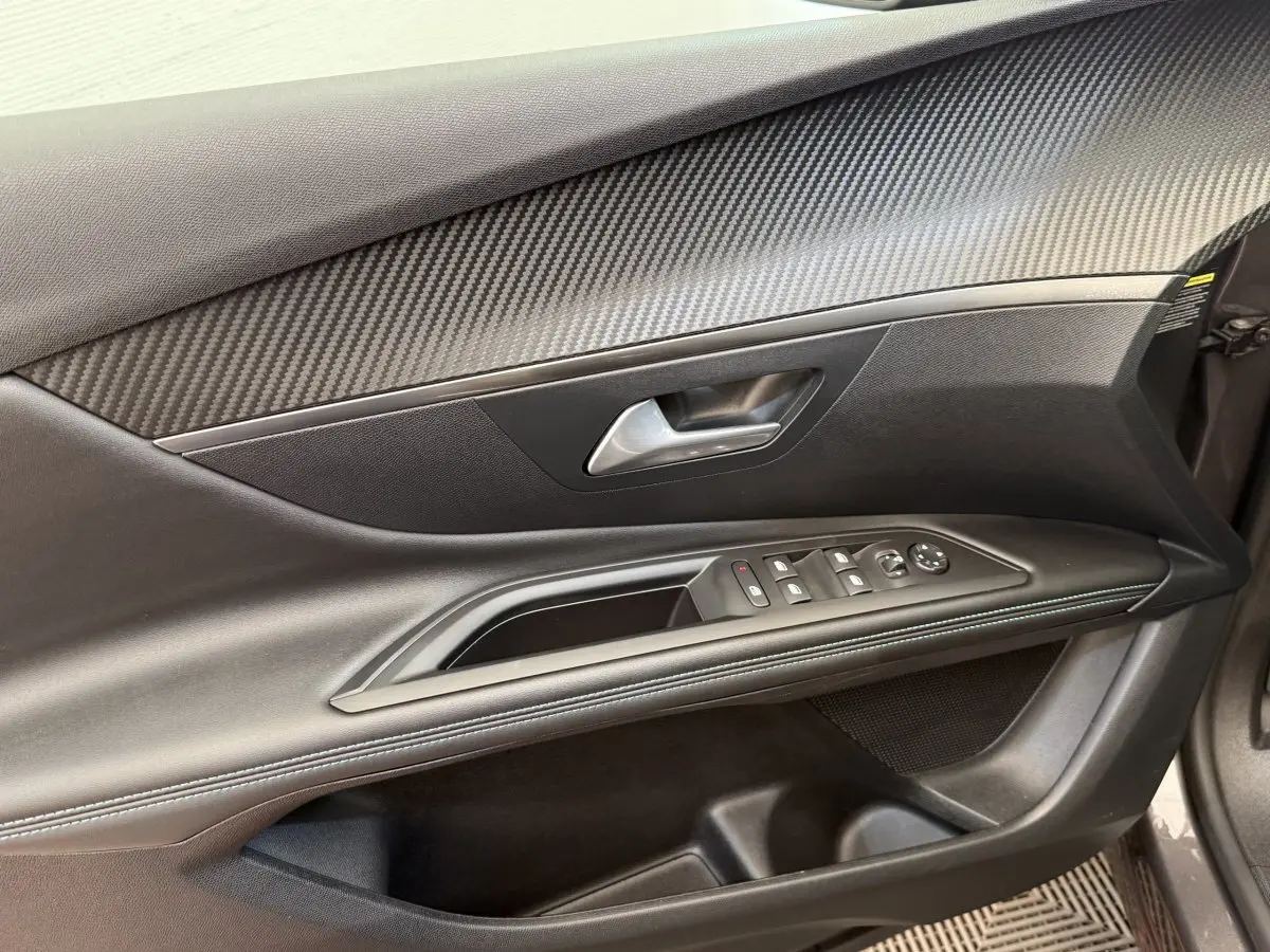 Gros plan sur la porte avant gauche du Peugeot 3008 gris foncé, avec commandes des vitres et insert effet carbone.