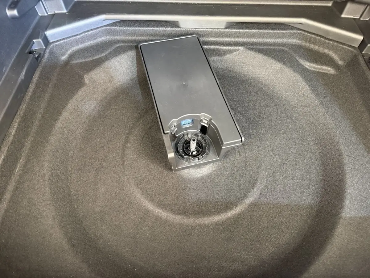 Vue rapprochée de la zone de rangement sous le coffre du Peugeot 3008 gris foncé, montrant un espace vide et un support central.