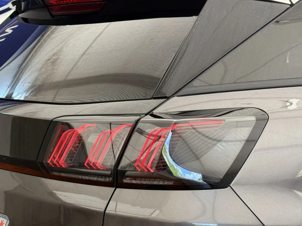 Gros plan sur le feu arrière droit rouge et noir du Peugeot 3008 gris foncé, avec reflet du toit en toile.