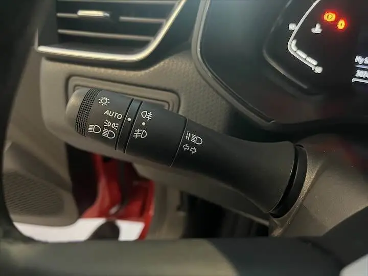 Gros plan sur la manette de commande des phares dans l'habitacle d'une Renault Clio V rouge flamme métal.