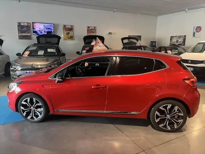 Profil côté gauche de la Renault Clio V rouge flamme métal, avec jantes alliage et vitres teintées en showroom.