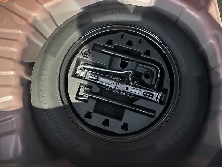 Gros plan sur la roue de secours et les outils de bord du coffre d'une Renault Clio V rouge flamme metal.