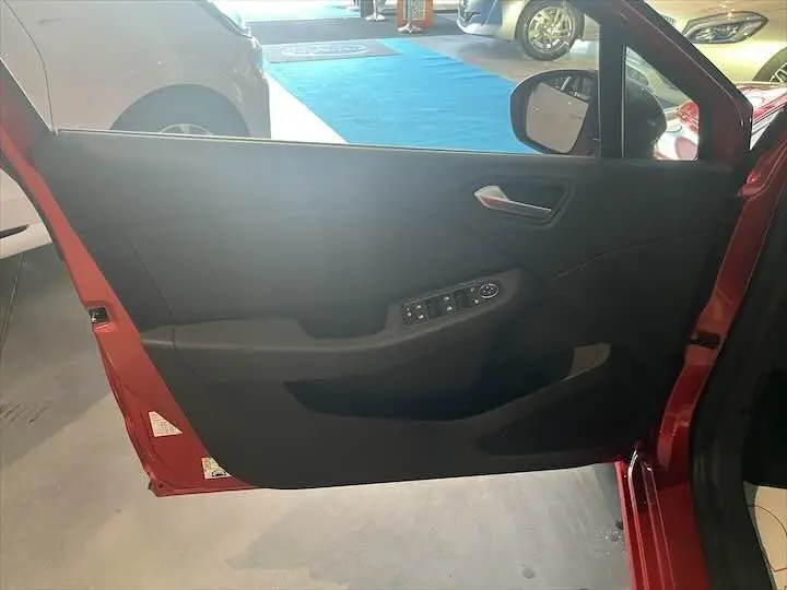 Vue rapprochée de la porte avant gauche rouge flamme métal d'une Renault Clio V 2021 avec commandes électriques.