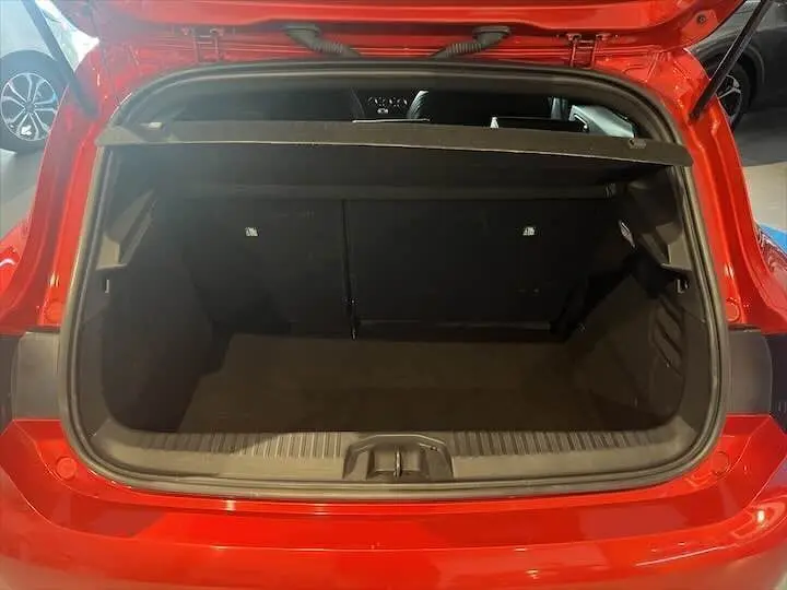 Coffre ouvert vu de l'arrière d'une Renault Clio V rouge flamme métal, montrant l'espace de chargement vide.