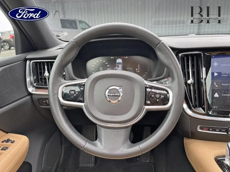 Vue rapprochée du volant cuir noir et tableau de bord numérique d'une Volvo V60 T8 gris Savile avec intérieur cuir brun.