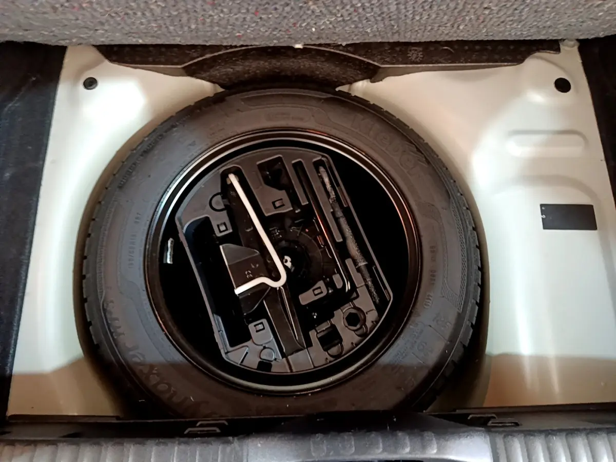 Gros plan sur la roue de secours en jante acier noire dans le coffre blanc d'une Citroën C3 blanche 2019.