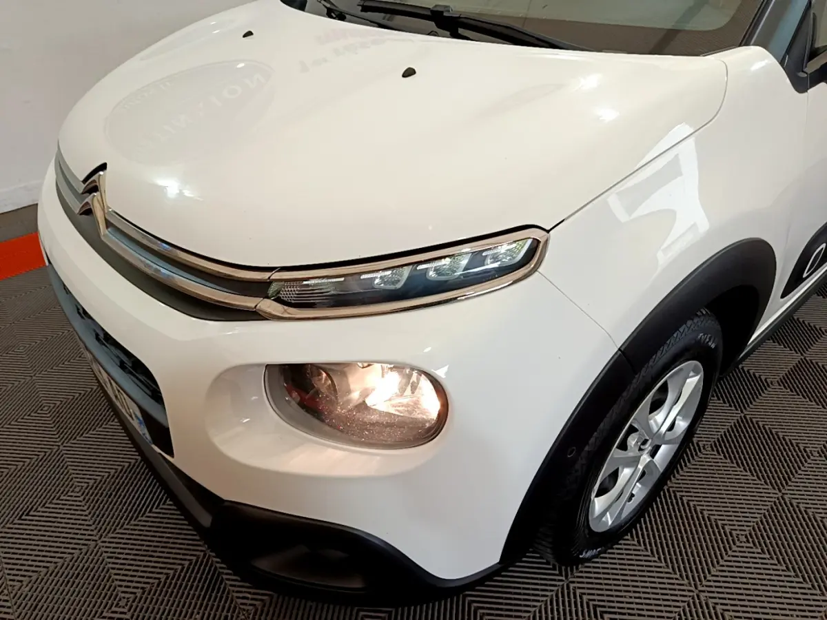 Vue 3/4 avant droit d'une Citroën C3 blanche avec phares allumés et jantes alliage visibles