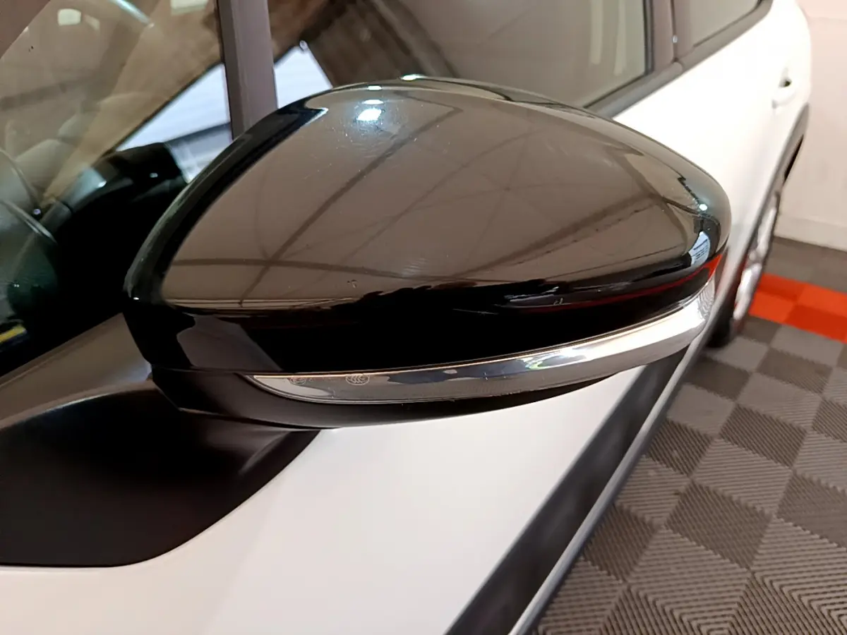 Rétroviseur noir brillant côté gauche d'une Citroën C3 blanche, vue rapprochée sur l'extérieur avant.