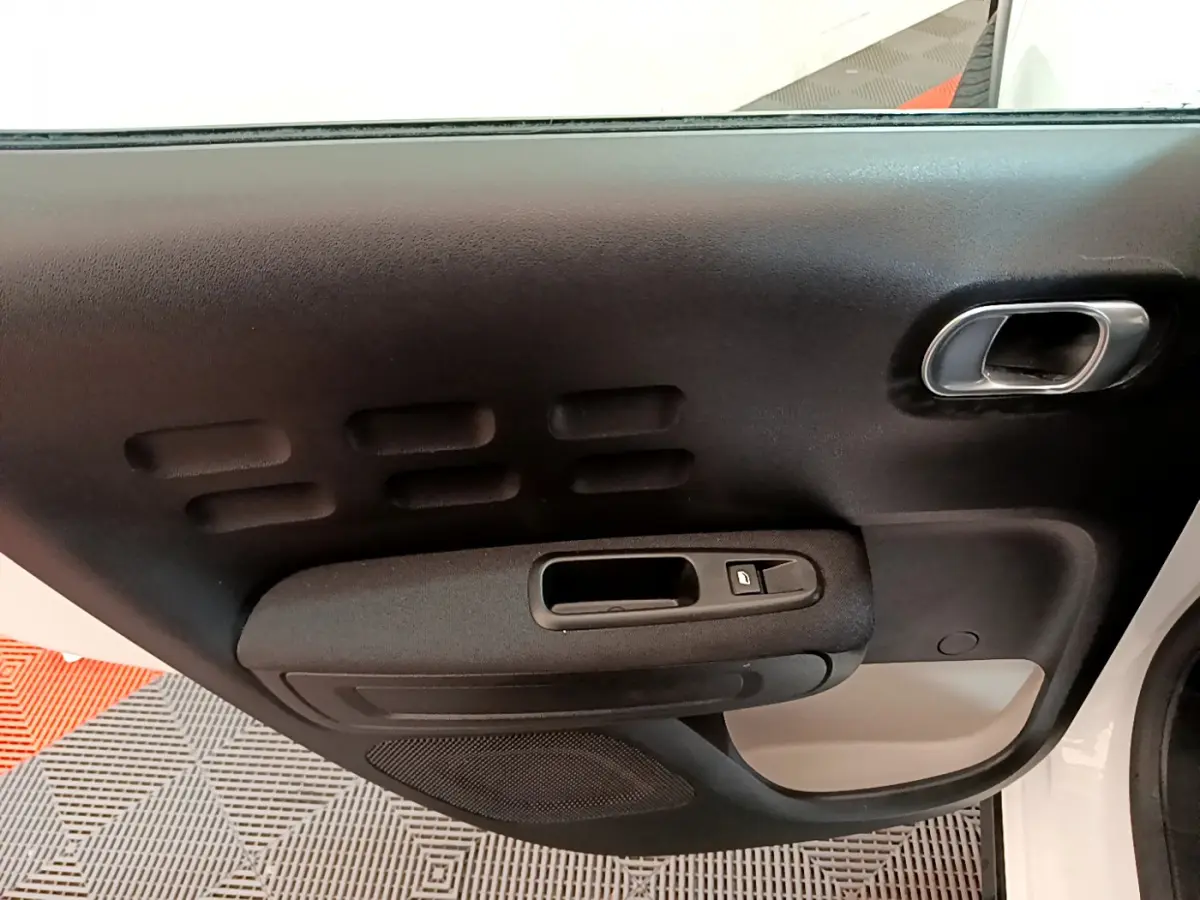Intérieur côté gauche de la porte avant d'une Citroën C3 blanche, avec poignée noire et bouton de verrouillage.