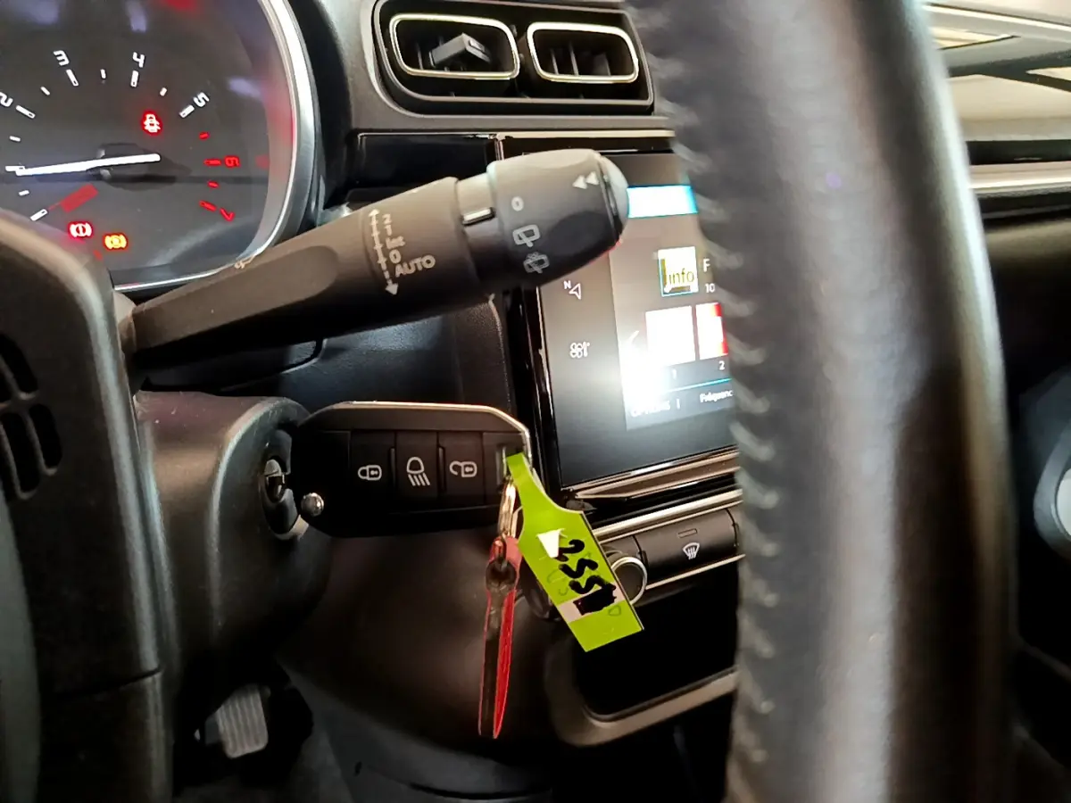 Vue rapprochée du tableau de bord et volant cuir noir de la Citroën C3 blanche avec clé insérée et écran tactile allumé.