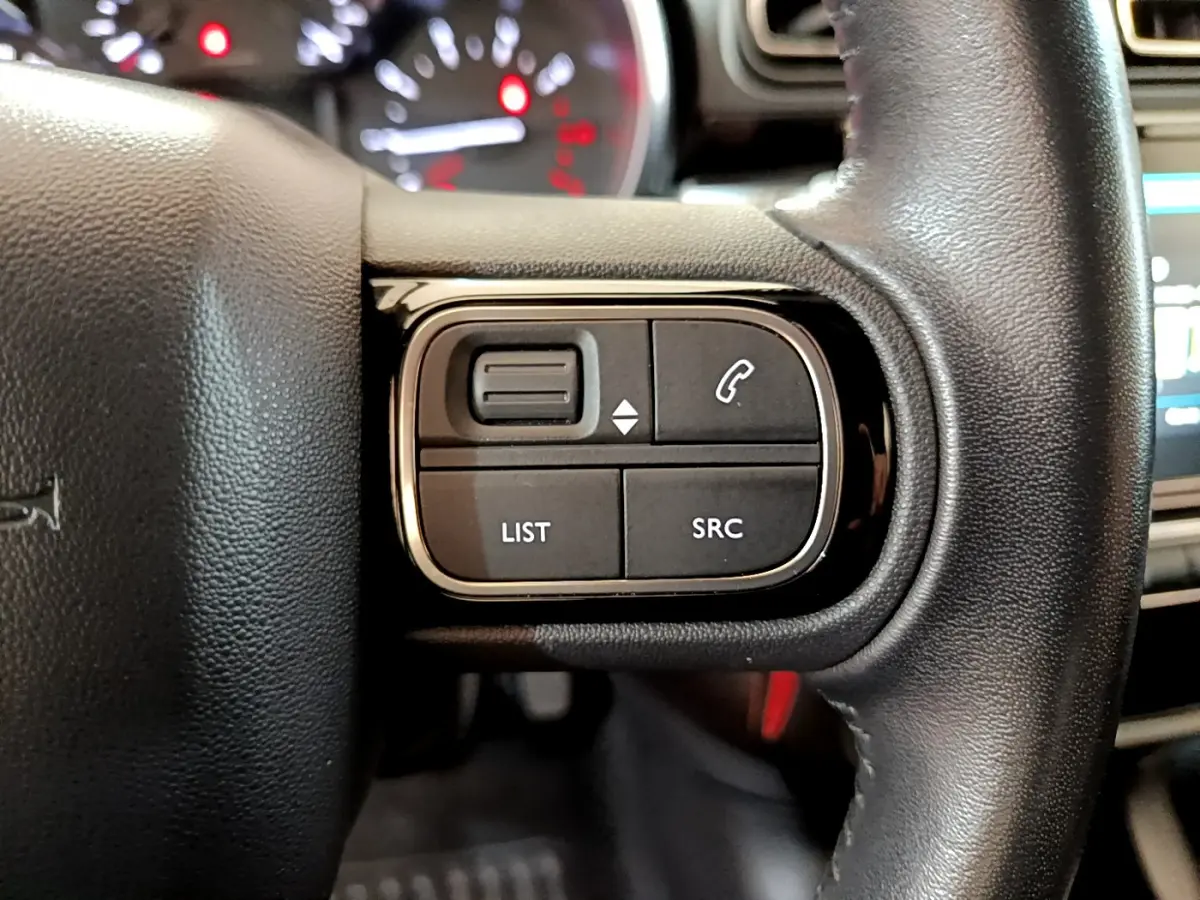 Gros plan sur les commandes gauche du volant cuir noir de la Citroën C3 blanche, avec boutons LIST et SRC visibles.