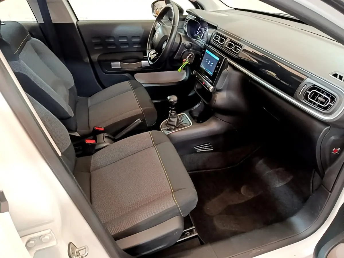 Intérieur avant droit de la Citroën C3 blanche 2019, sièges noirs, tableau de bord avec écran tactile et volant cuir.