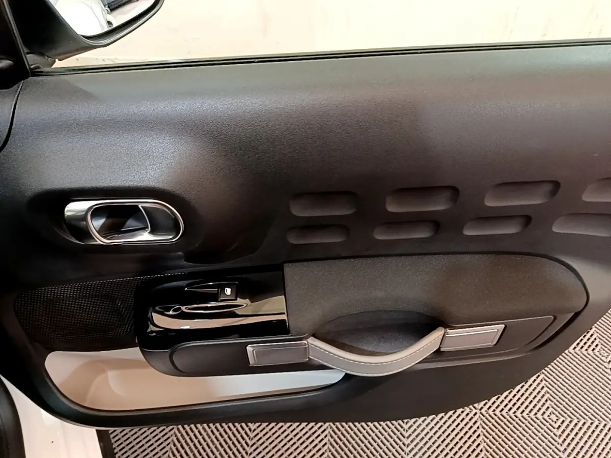 Gros plan sur la porte côté conducteur noire avec poignée argentée et commandes électriques d'une Citroën C3 blanche.